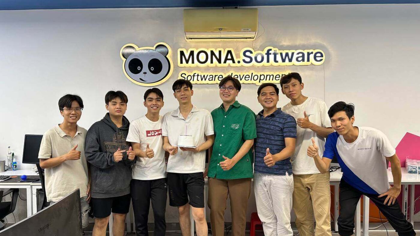 Đội ngũ MONA Software chụp ảnh trước logo công ty tại văn phòng